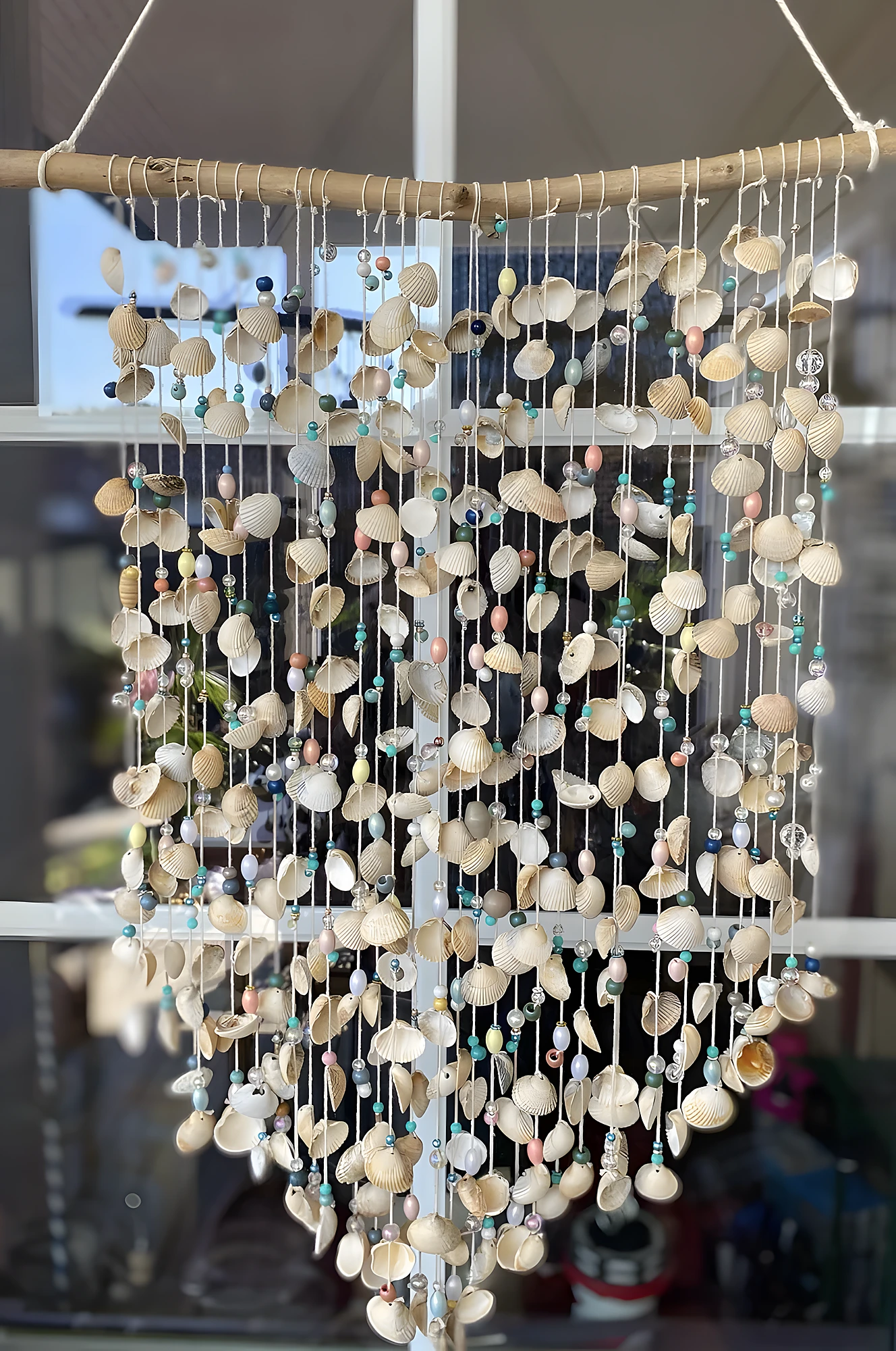 Large hanging shell curtain with driftwood, cotton cord, and pastel beads; intermediate craft requiring lots of threading.