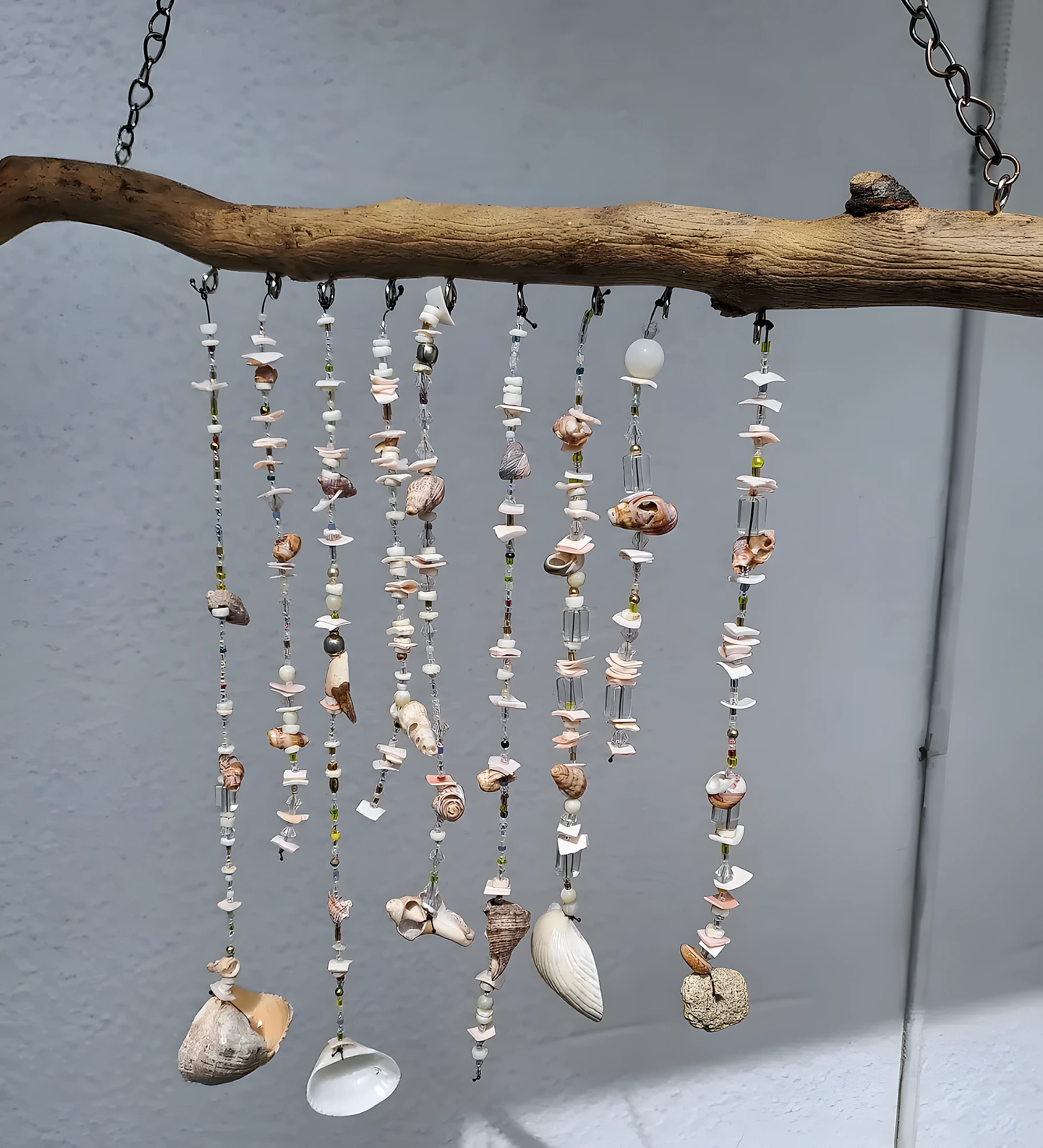 Handmade wind chime with driftwood, shell beads, and hanging strands; intermediate craft using drilling, knotting, and balancing.